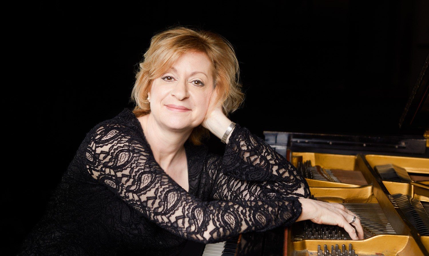 Dr. Marjorie Hohlstein, piano teacher in Lakewood Ranch, smiling beside her grand piano.